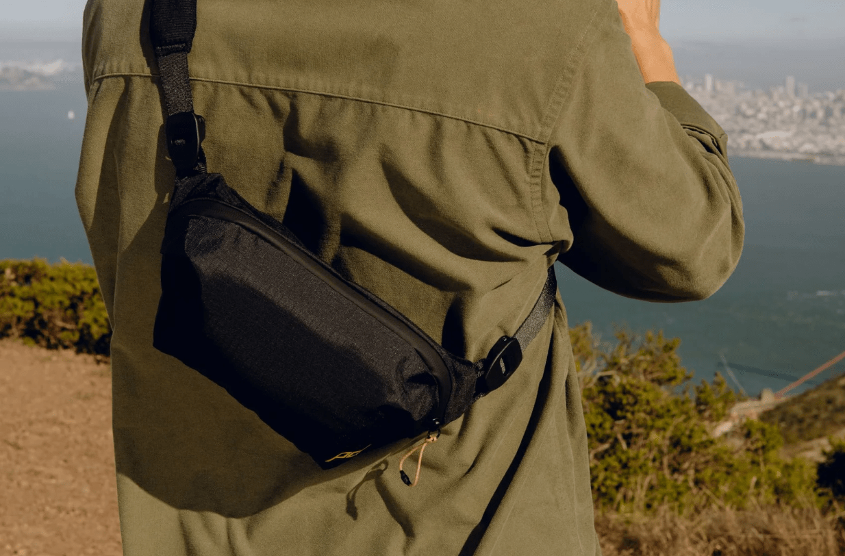 Person with camera looking out at landscape with sling across their back.