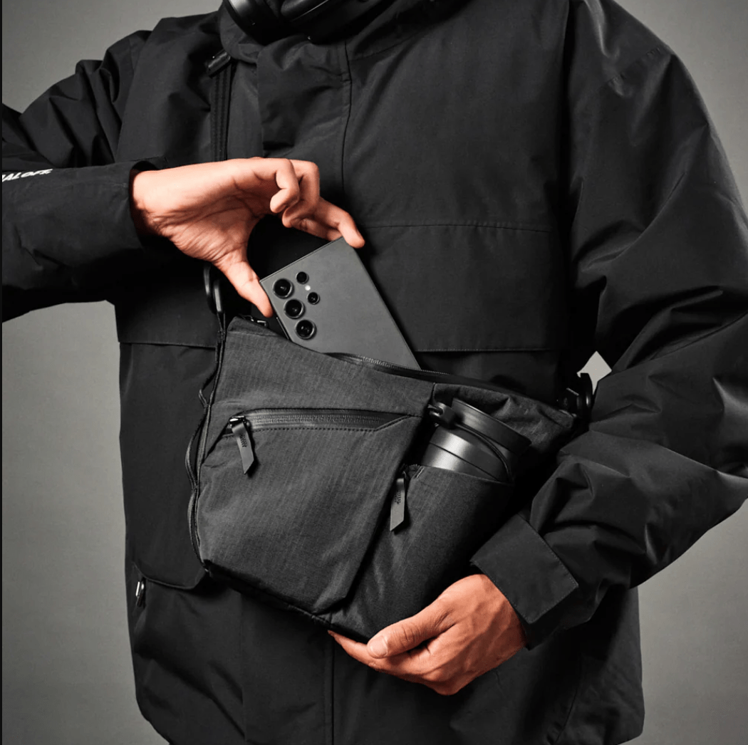 Person putting phone into black slink that also has a water bottle and several pockets