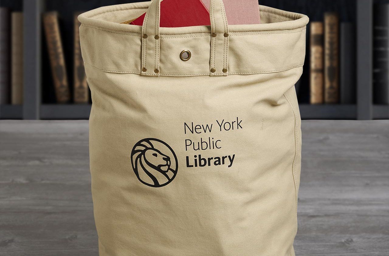 Large beige tote bag filled with books with shelves in the background.