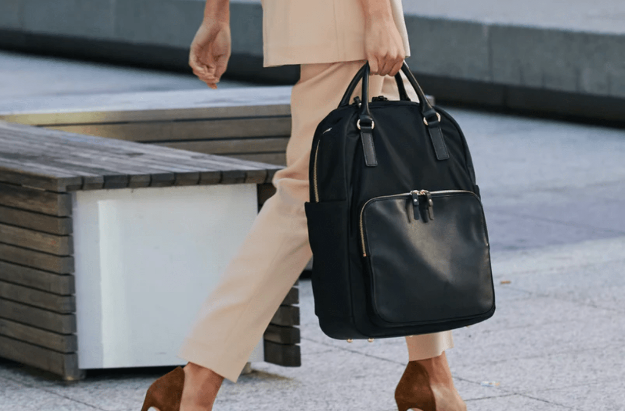 Woman walking down urban street holding backpack in one hand