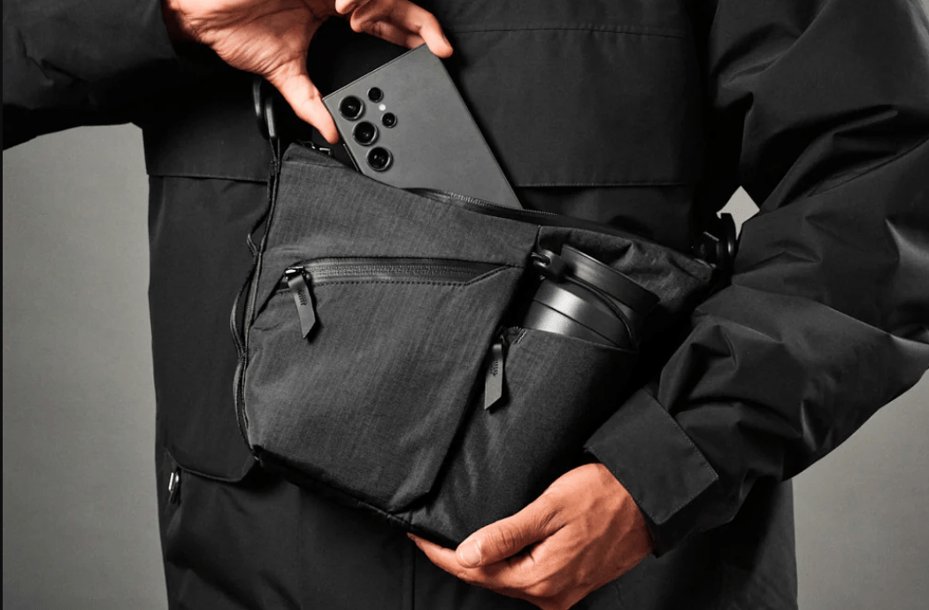 Person putting phone into black slink that also has a water bottle and several pockets