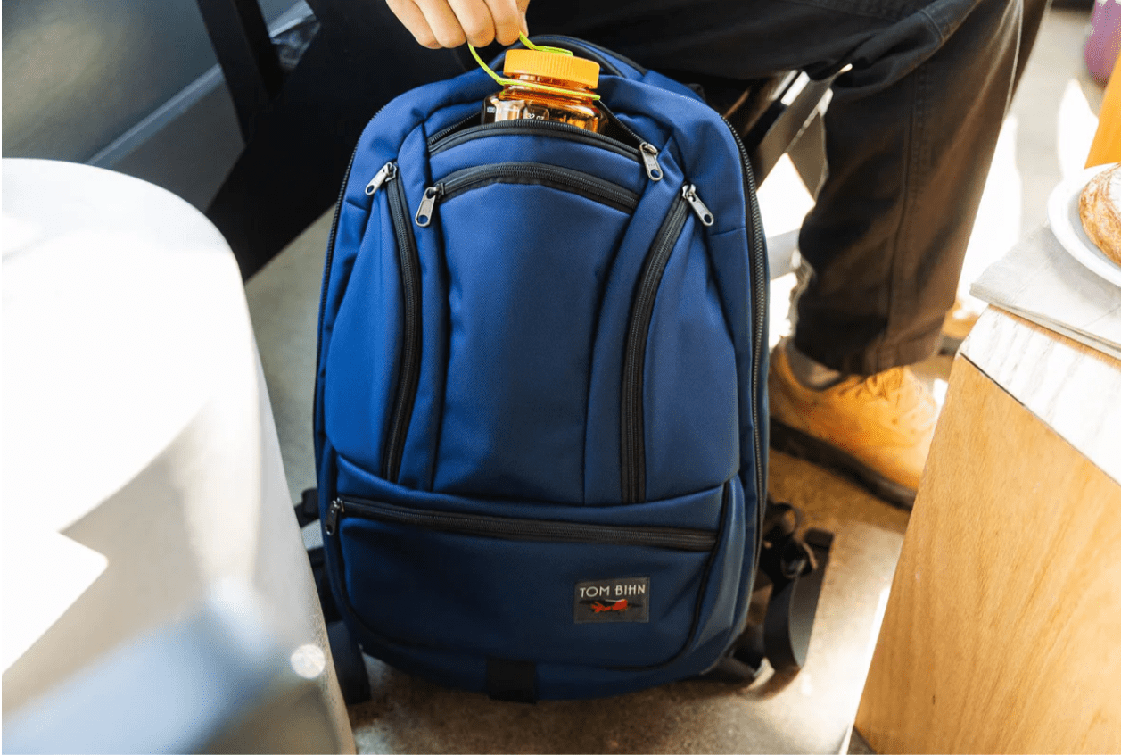 Blue backpack with somebody putting a water jug inside the middle pocket