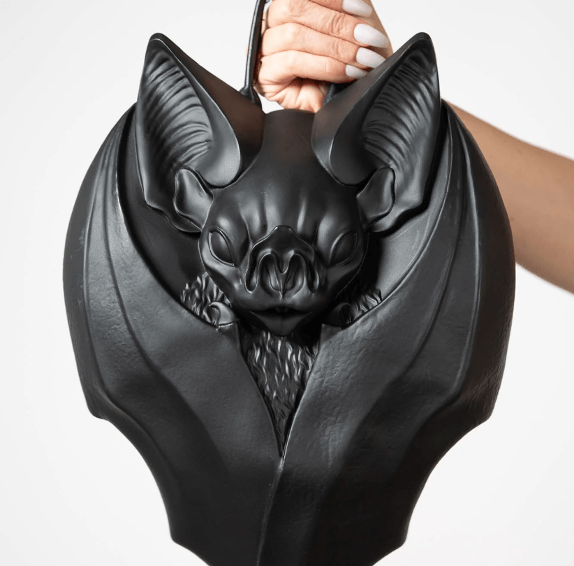 Hand holding handbag in the shape of a bat with its wings folded