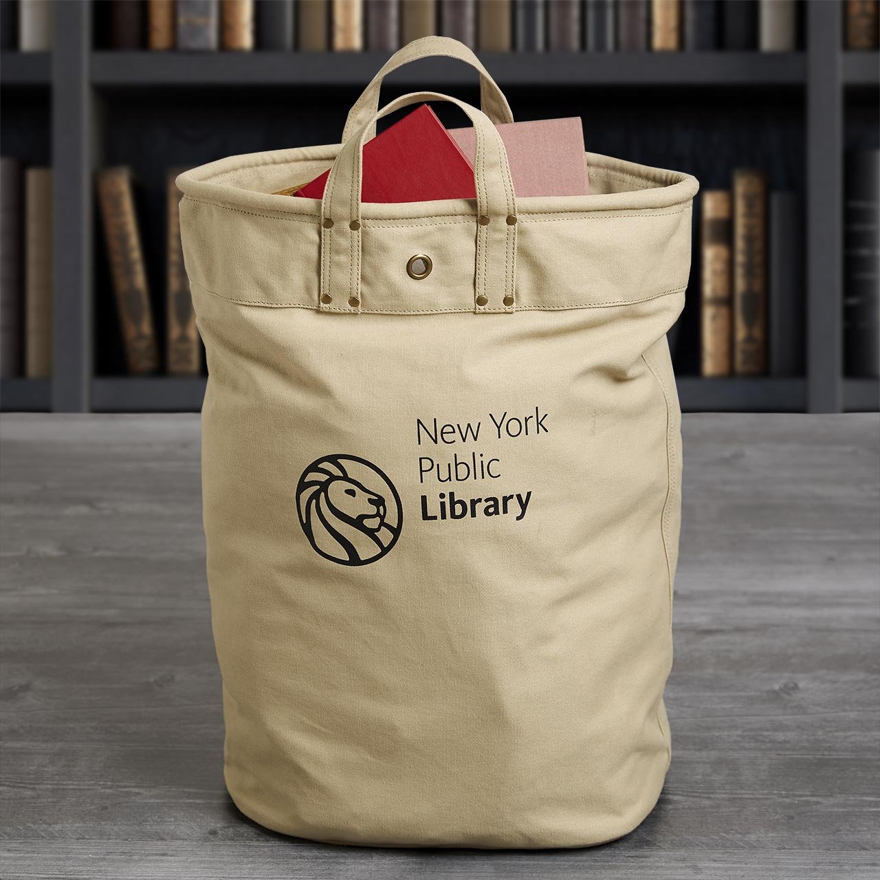 Large beige tote bag filled with books with shelves in the background.