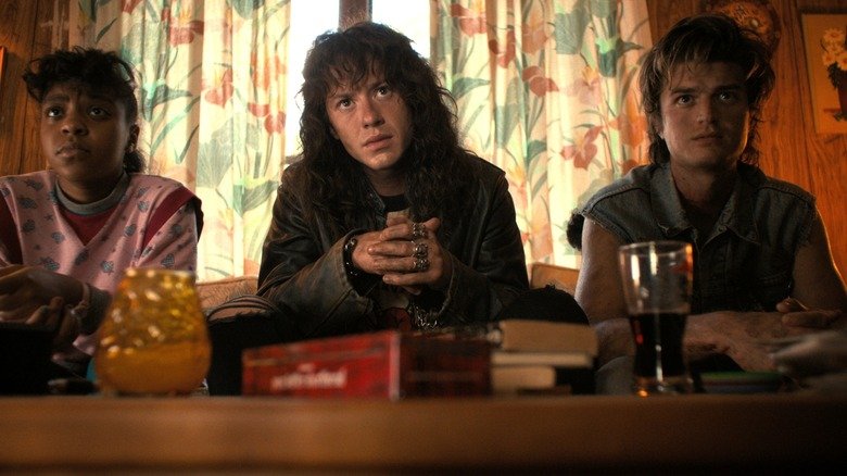 Irika, Eddie and Steve are sitting on a sofa in strange things season 4