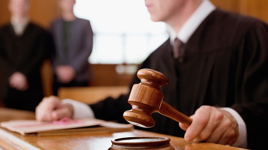 The judge holds clothing in the courtroom