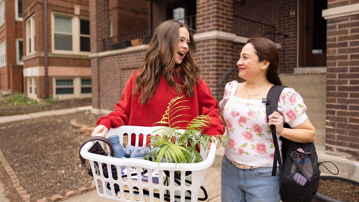 The mother and her daughter linking joy while transferring property to a magical brick building, and it is assumed that a university housing. A girl carrying a washing basket full of room materials.