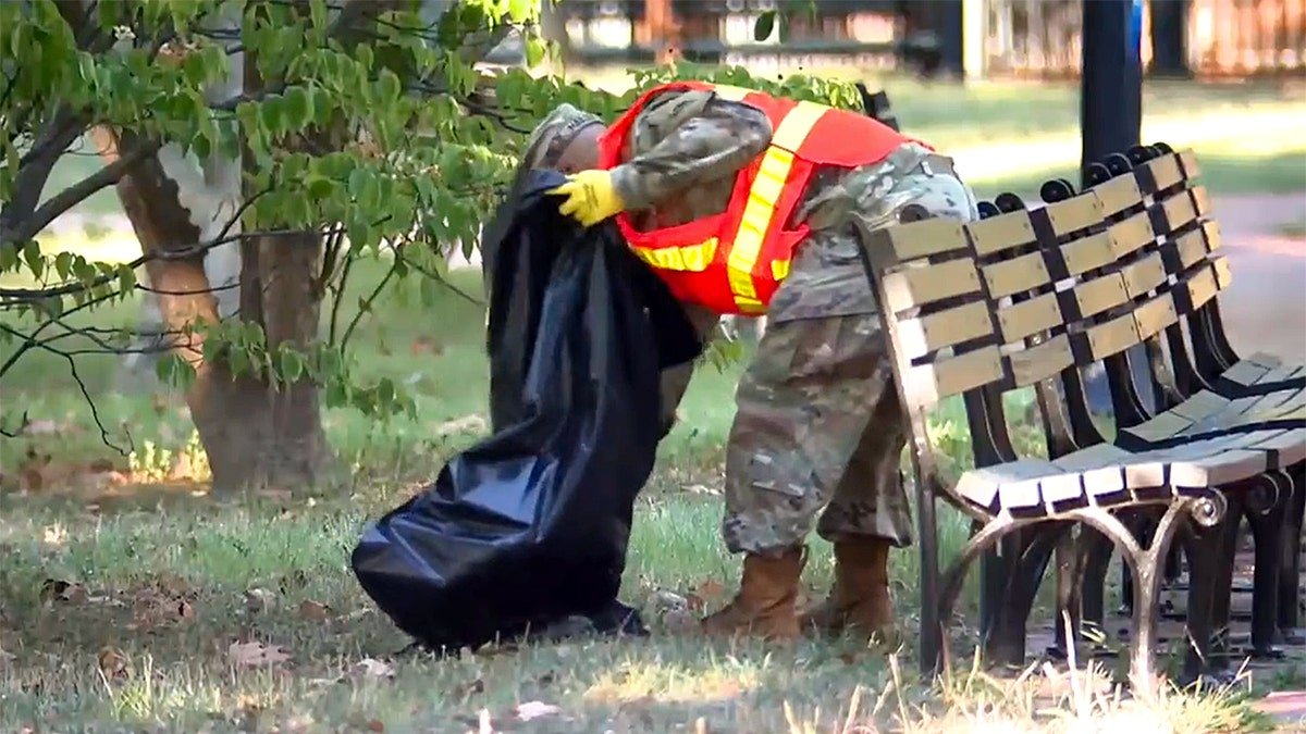 The goalkeeper member bends to capture garbage near the seats in Lavait Park