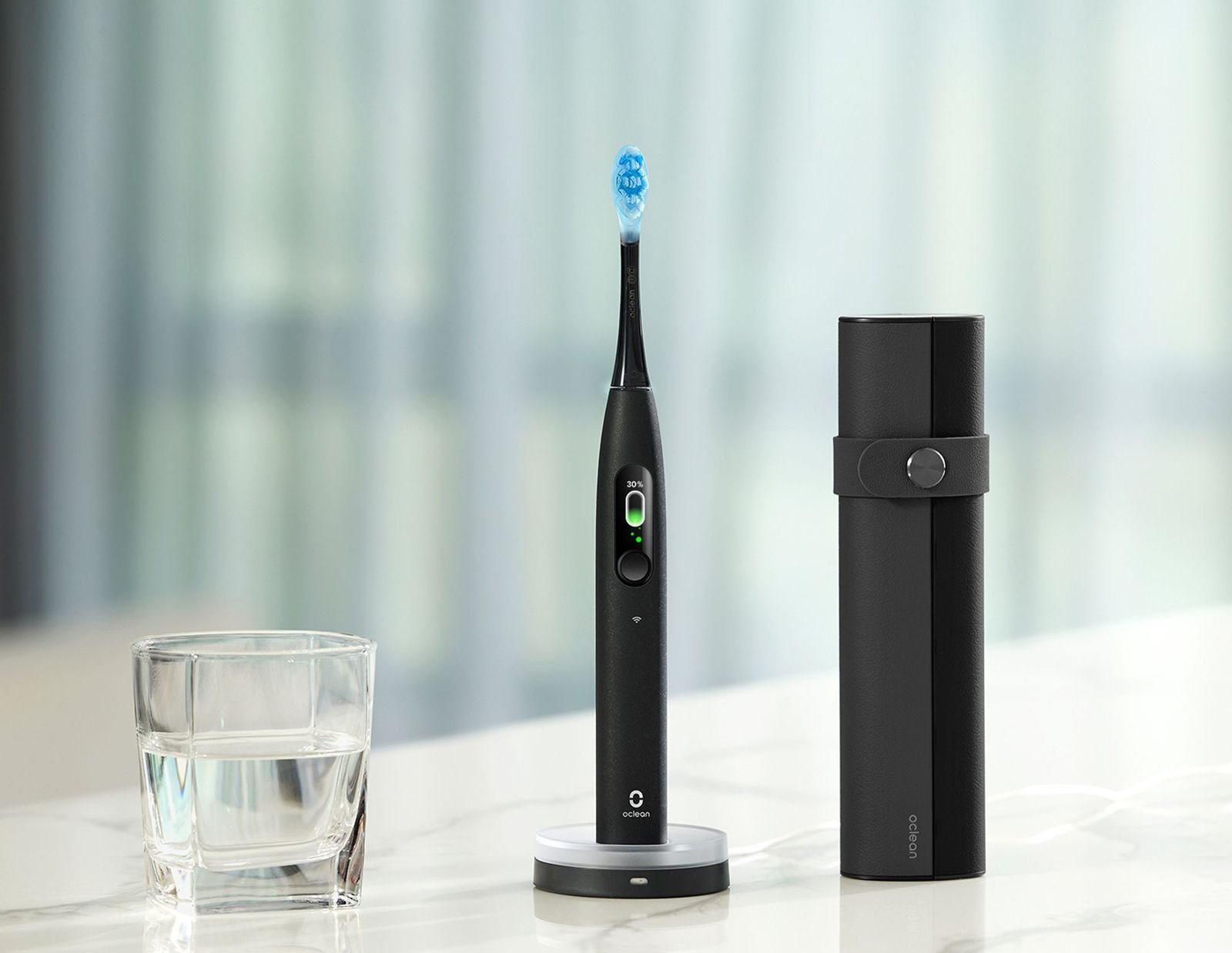 Black electric toothbrush sitting on a marble table next to a cup of water and a black pregnancy