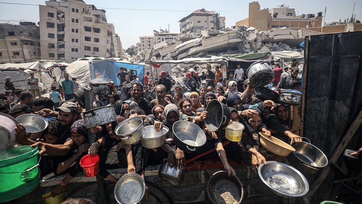 Palestinians who hold the articles gather to receive hot meals, on July 23, 2025.