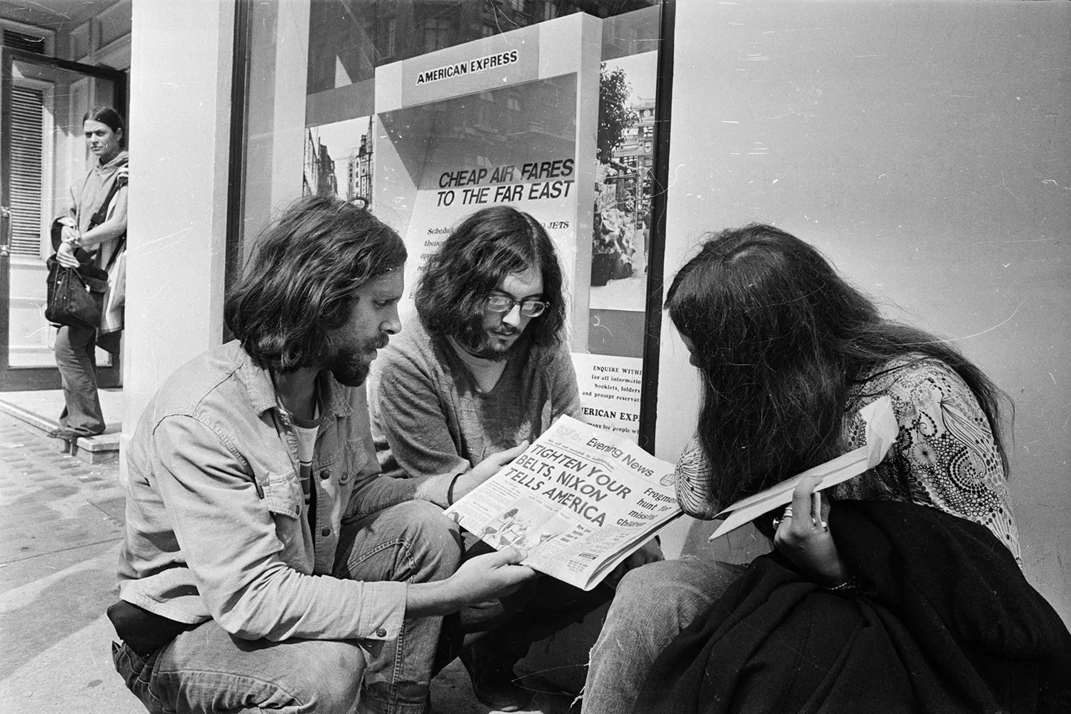 A historic image of three young people reading a newspaper on the street in London. The headline reads "Tighten your belts, Nixon tells America."