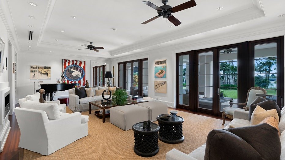 The living room includes multiple white sofas and French doors that lead to the backyard.