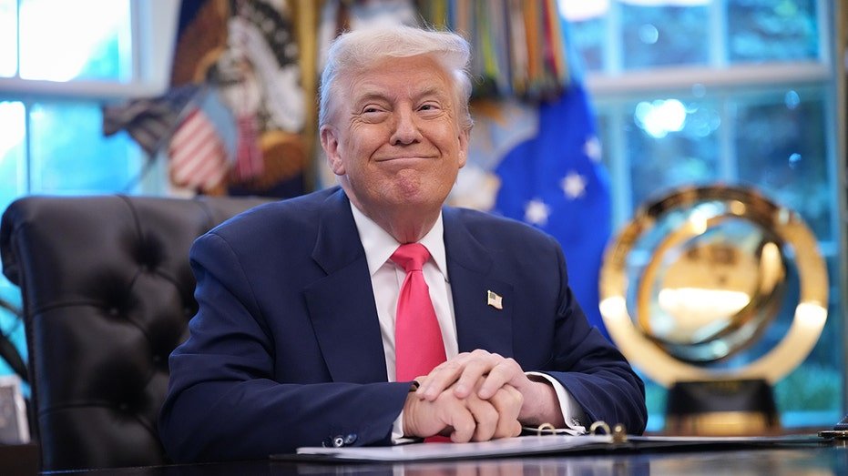 President Donald Trump smiles while sitting on his office in the Oval Office