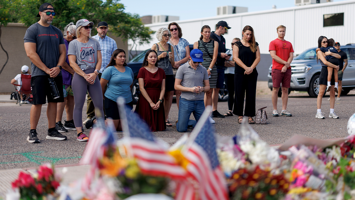 A group of people praying outside a temporary memorial for Charlie Kirk, which consists of American flowers and flags