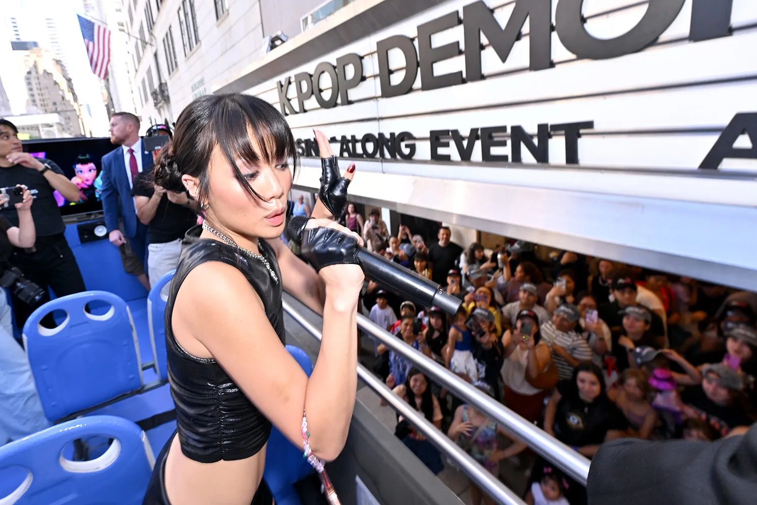 A woman at the top of a leather crop and leather fingers carrying a microphone singing over the bus. A crowd looked under the belows of it.