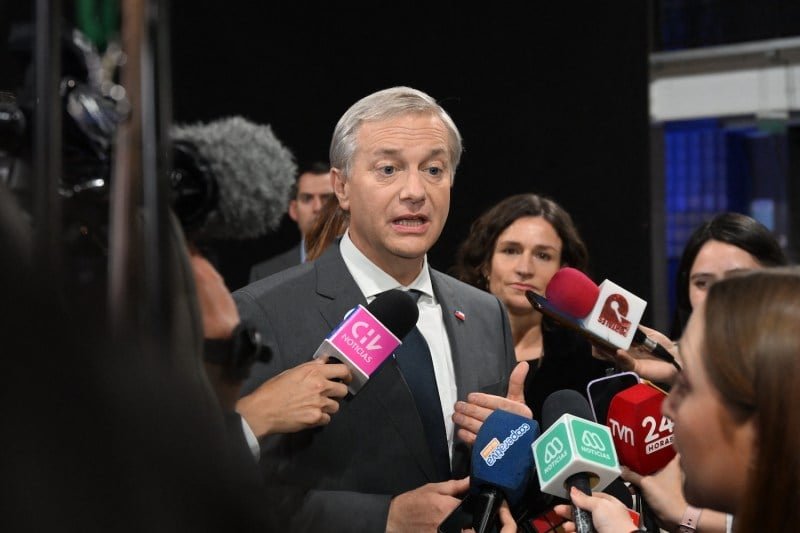 A man wears a suit talking to journalists who hold the microphones in front of him.