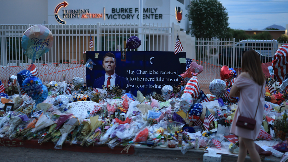 A woman wears a pink dress approaching a temporary memorial to Charlie Kerk outside the Turning Point Usa office in Arizona in dusk