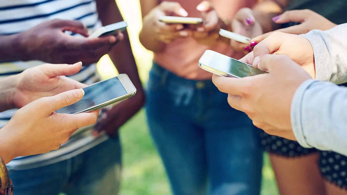 A group of children standing in a circle, all using their cell phones, focusing in the center.