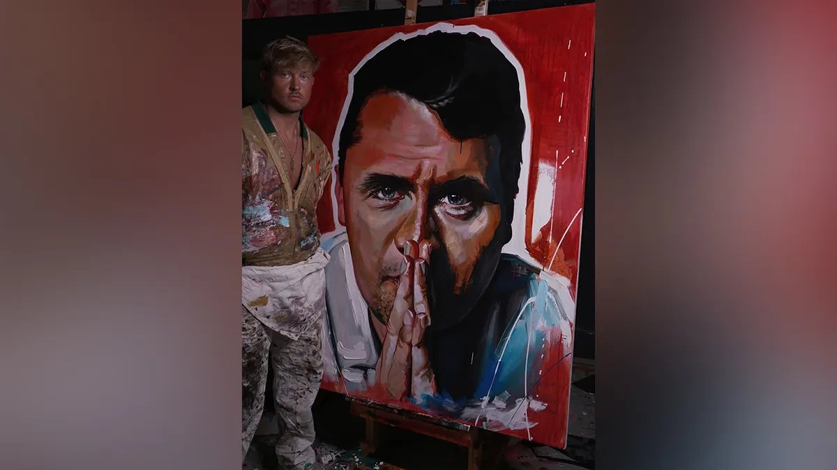 Sam Ryan poses next to his portrait of Charlie Kirk.