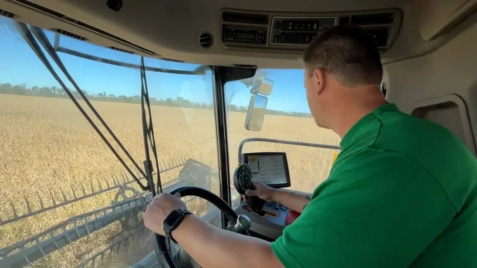 A farmer operates a combine harvester while harvesting soybeans in Illinois.