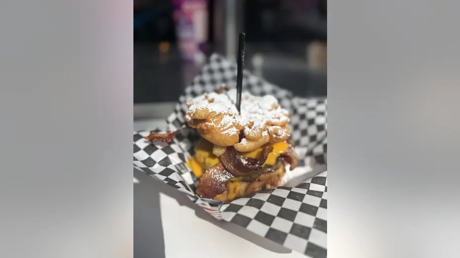 Grilled hamburger patty with crispy bacon and queso cheese sauce, sandwiched between two buns covered in powdered sugar.