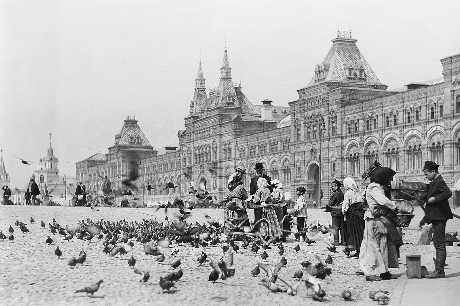 A black and white photo of a public square in Moscow with many people and birds.
