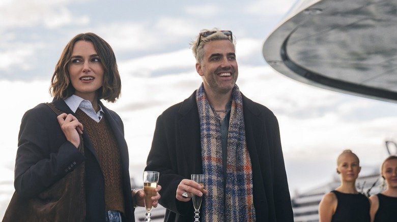 Lou and Adam hold champagne glasses and look around on the ship in The Woman in Cabin 10