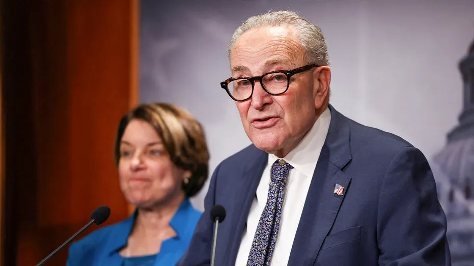 Chuck Schumer speaks and Amy Klobuchar stands behind him