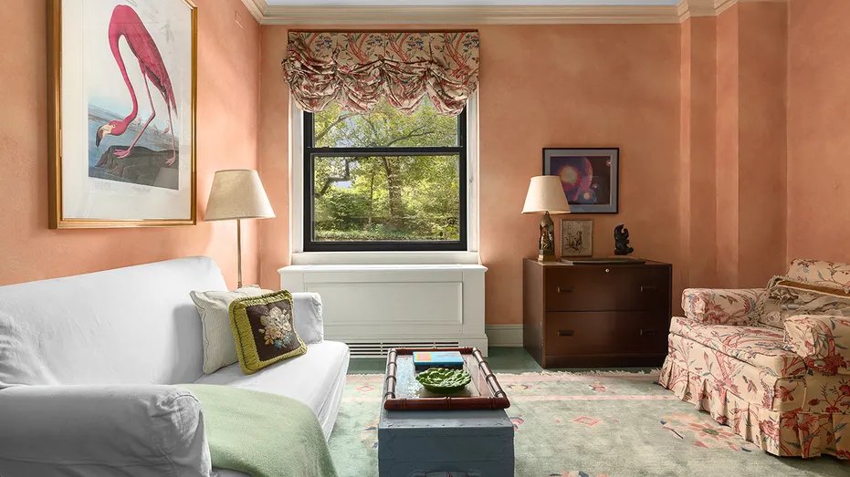 A living room with pink walls and a window overlooking the outside.