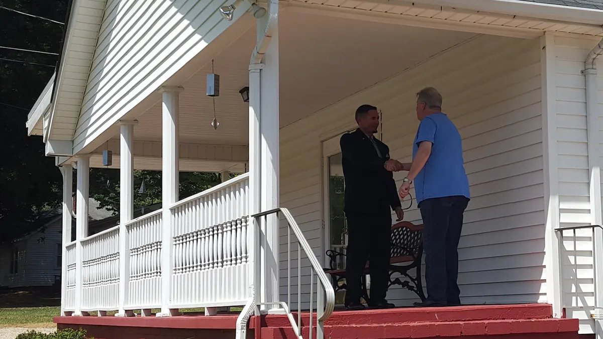 A priest and a man shake hands outside on the church balcony.