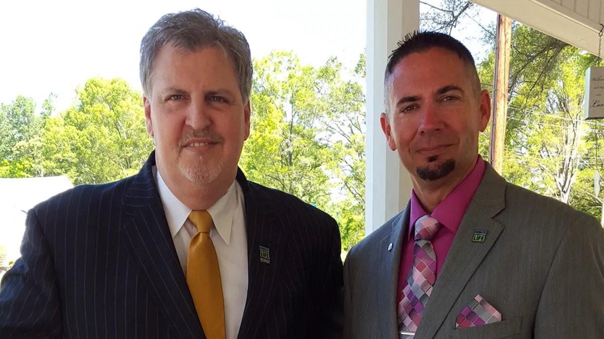 Two men standing outside and smiling at the camera.