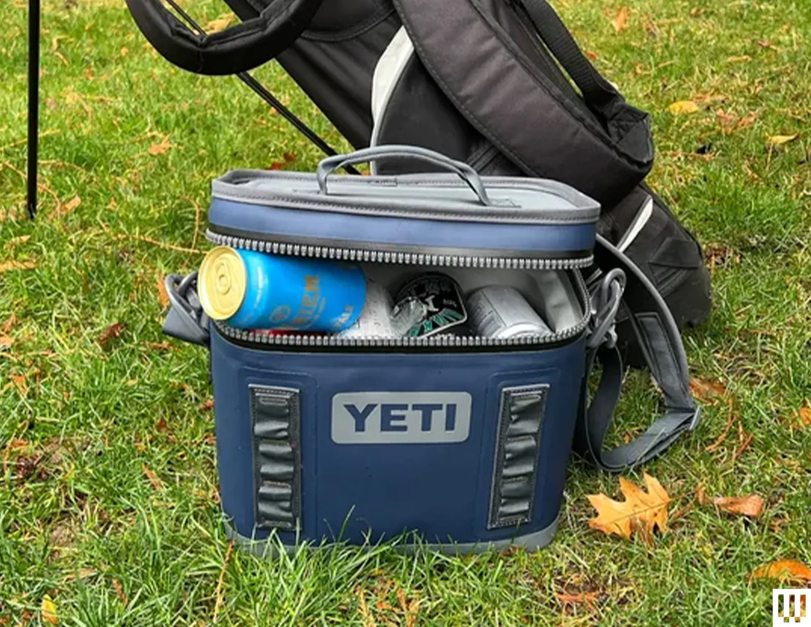 Yeti Hopper Flip 8 Cooler a blue padded device holding canned beverages leaning against a black golf bag sitting in the...
