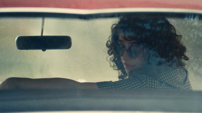 Rachel sits in the car and looks out the back window at Marty Supreme