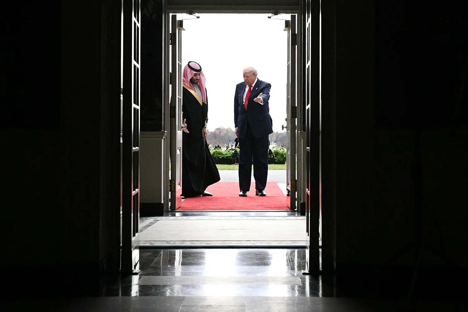 Trump and Mohammed bin Salman gesture to each other at a doorway.