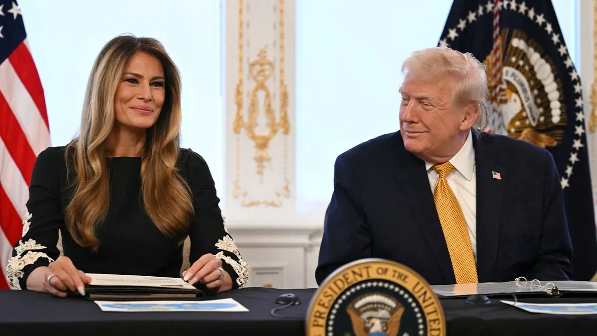 First Lady Melania Trump smiles as she sits next to President Donald Trump, who smiles at her