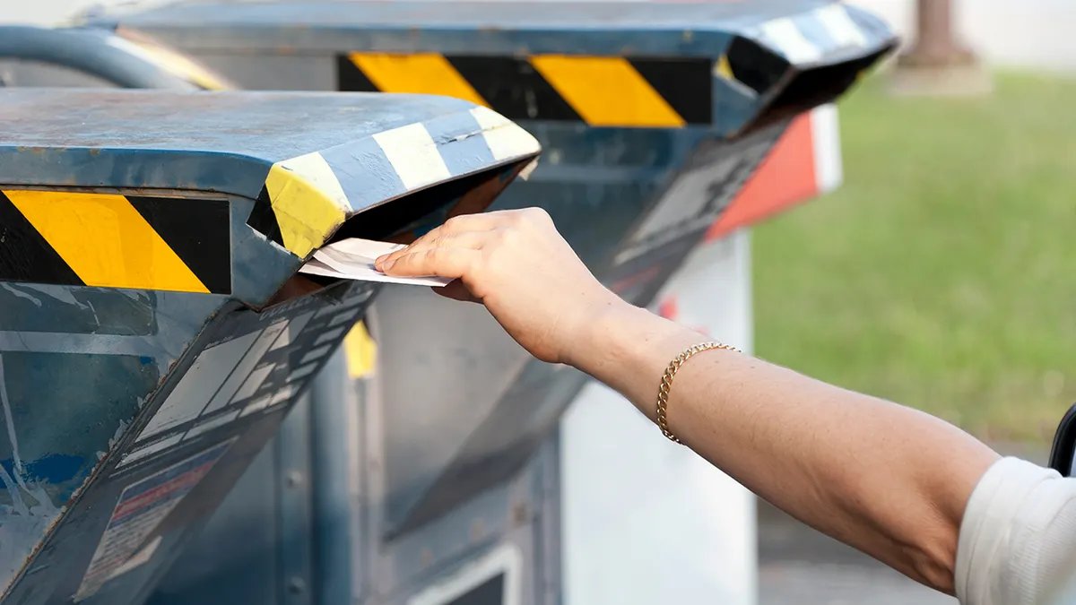 A person places mail into a residential mailbox slot into a metal community mailbox.