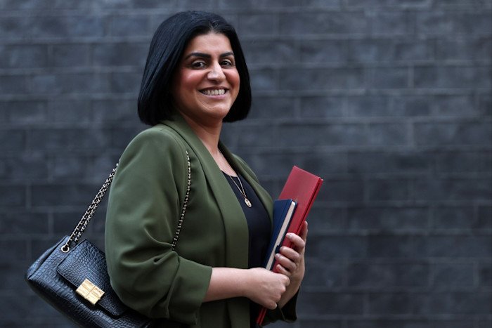 Shabana Mahmoud smiles as she carries the documents and exits the building, wearing a green jacket and carrying a black handbag