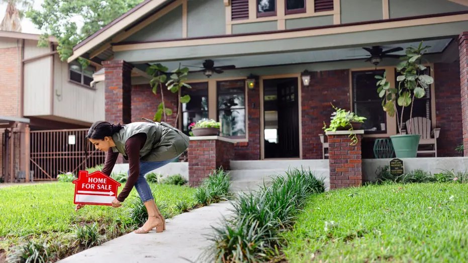 A real estate agent with a "For sale" Sign in front of the house.