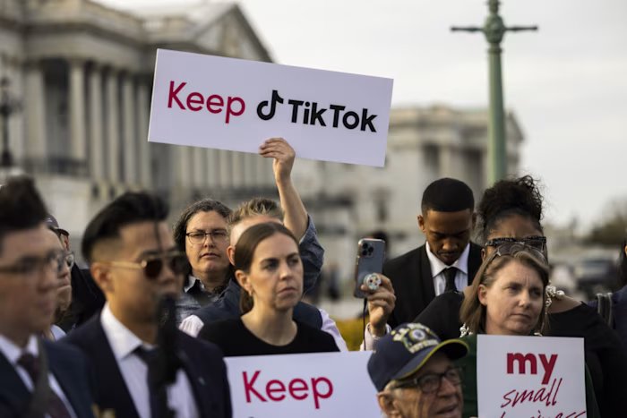 A group of people stand outside the Capitol, one of them holding a sign that reads 