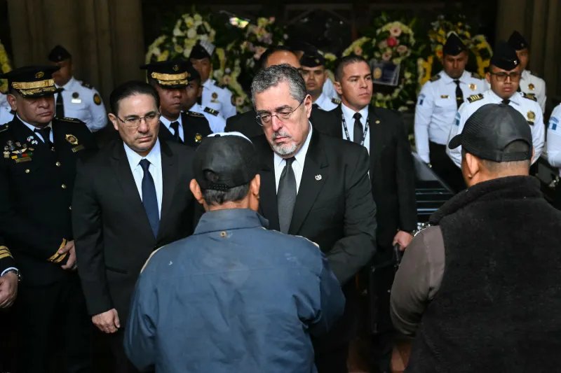 Surrounded by uniformed military personnel, Guatemalan President Bernardo Arevalo shakes a man's hand.