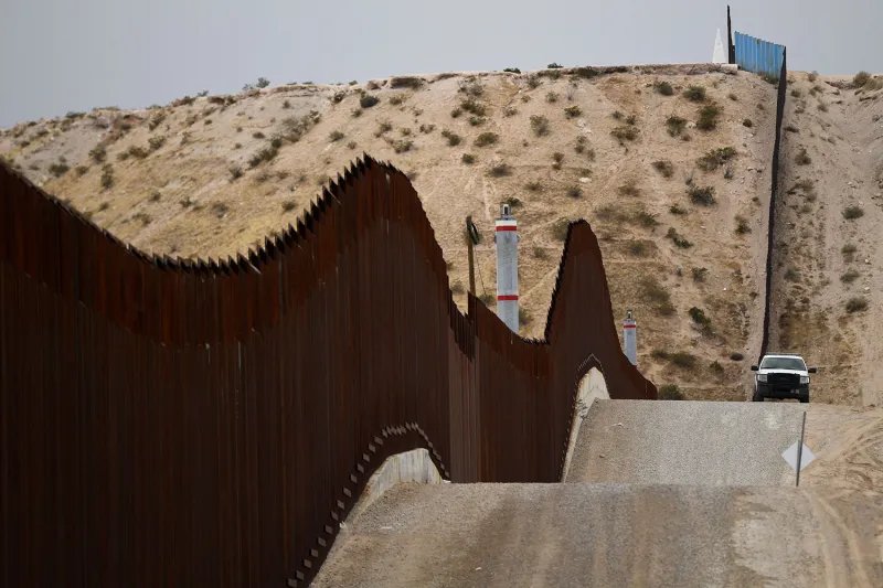 A US Border Patrol vehicle near the border wall on some hills.