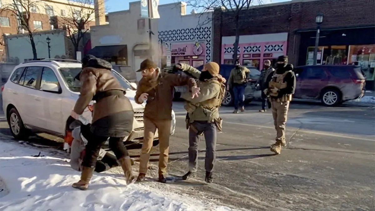 A law enforcement officer sprays a chemical spray toward a man during a confrontation on a city street.