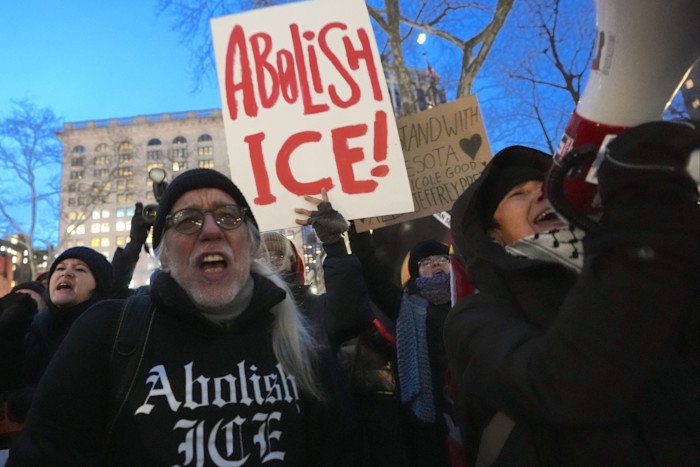 Protesters wearing winter clothes carry signs with the words: 