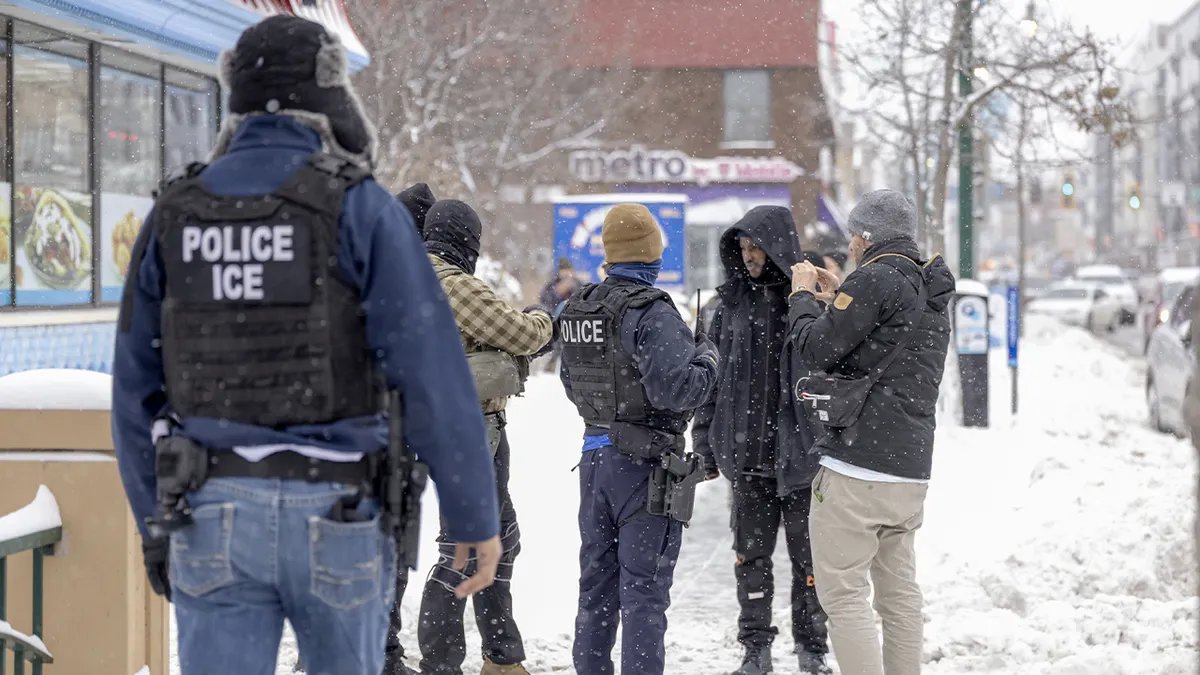 Federal officers speak with a man on a busy commercial street as passersby look on.